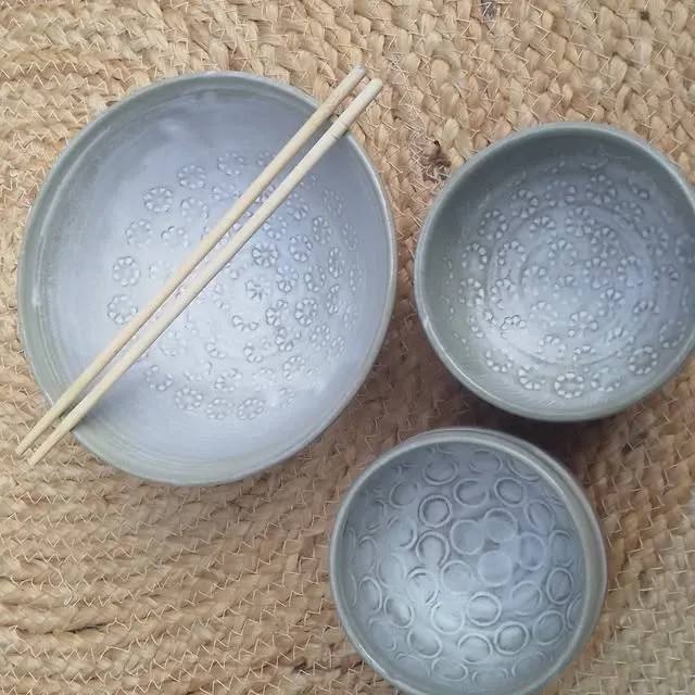 Trois bols à l’intérieur gris-bleu imprimé de motifs, avec des baguettes, sur un tapis de raphia