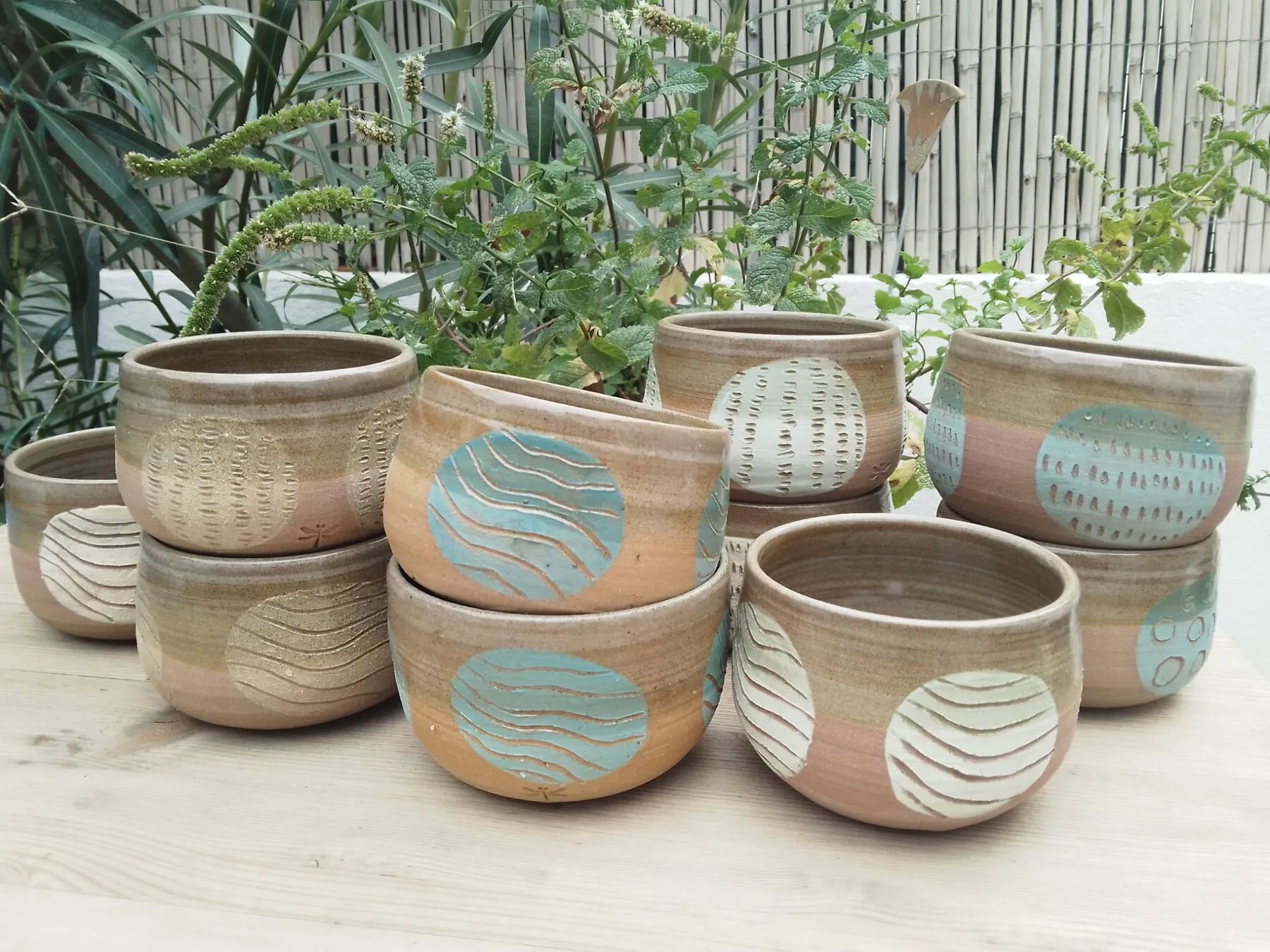 Bols empilés sur une table au jardin, décor de cercles gravés turquoise et blanc, signés d’une libellule